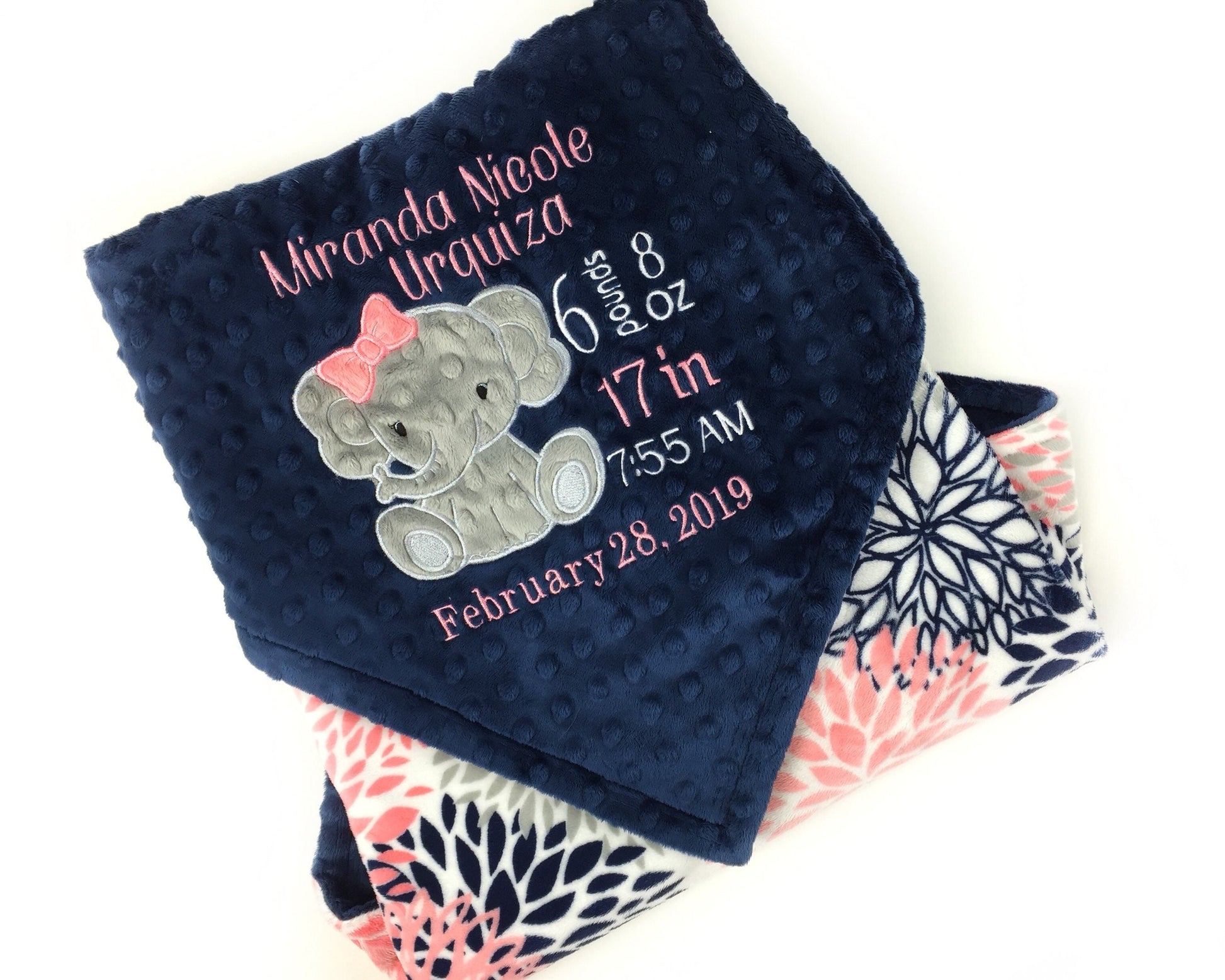 Baby blanket with a gray elephant applique and birth stats in coral and white. Blanket has navy dimple dot on one side with the elephant. The other side is smooth coral and navy floral minky. This is a beautiful soft blanket for baby to snuggle.